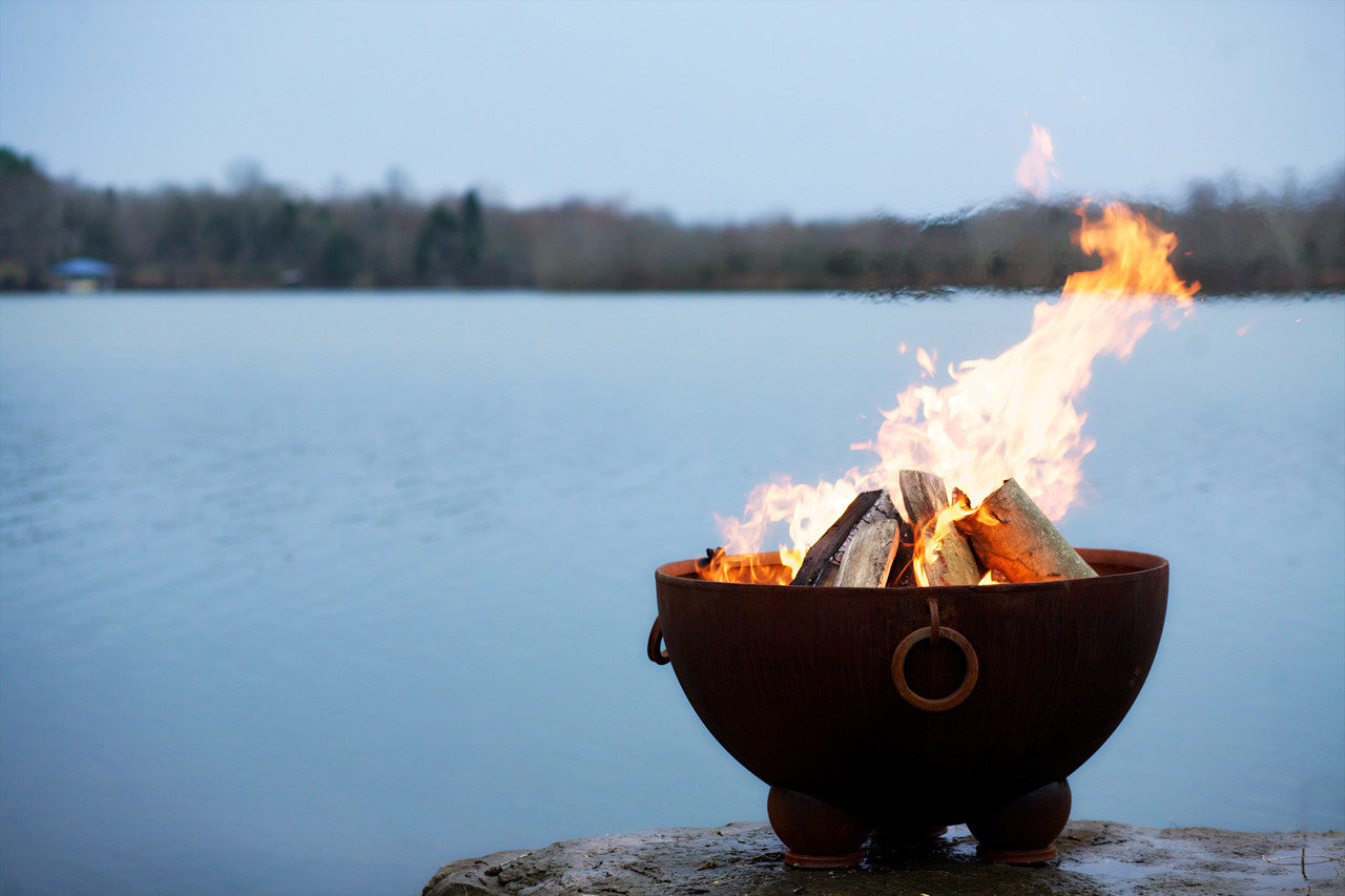 Magnificent artist scupture Fire pit bowl with burning wood by a lake at sunset