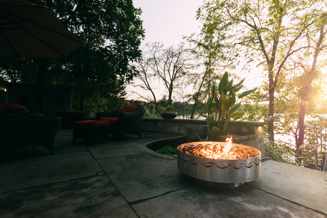 Fire pit on a patio with trees and sunset in the background