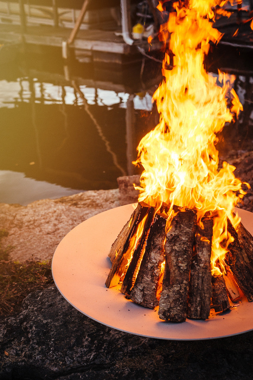 Fire pit with flames burning on a stone surface near water