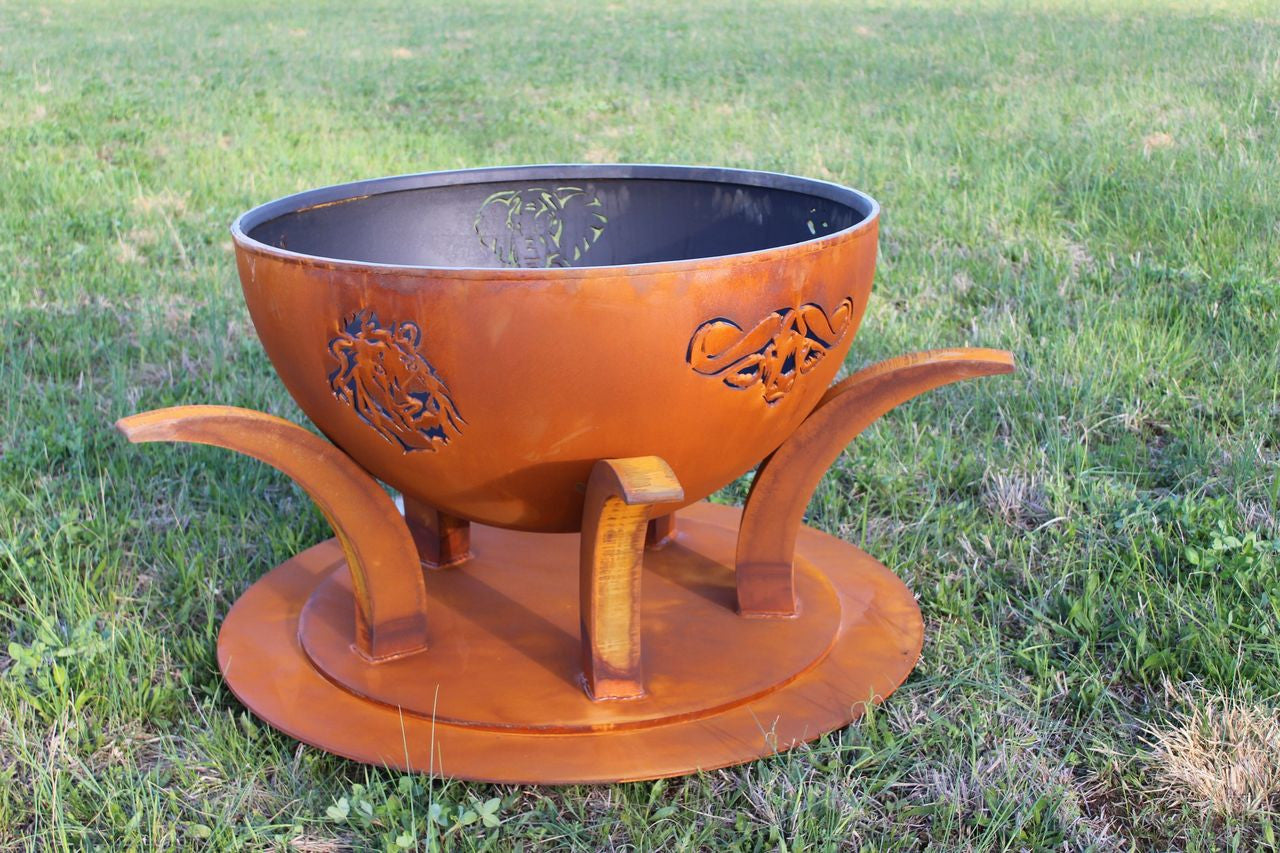 Rust-colored metal fire pit with decorative design on a grassy background