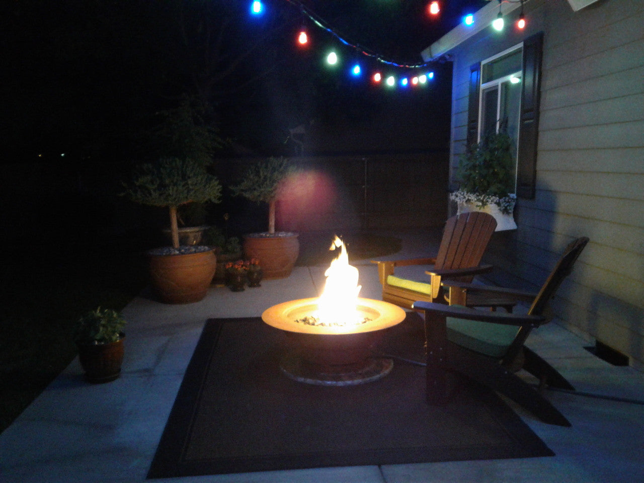 Fire pit on a patio with decorative lights and potted plants