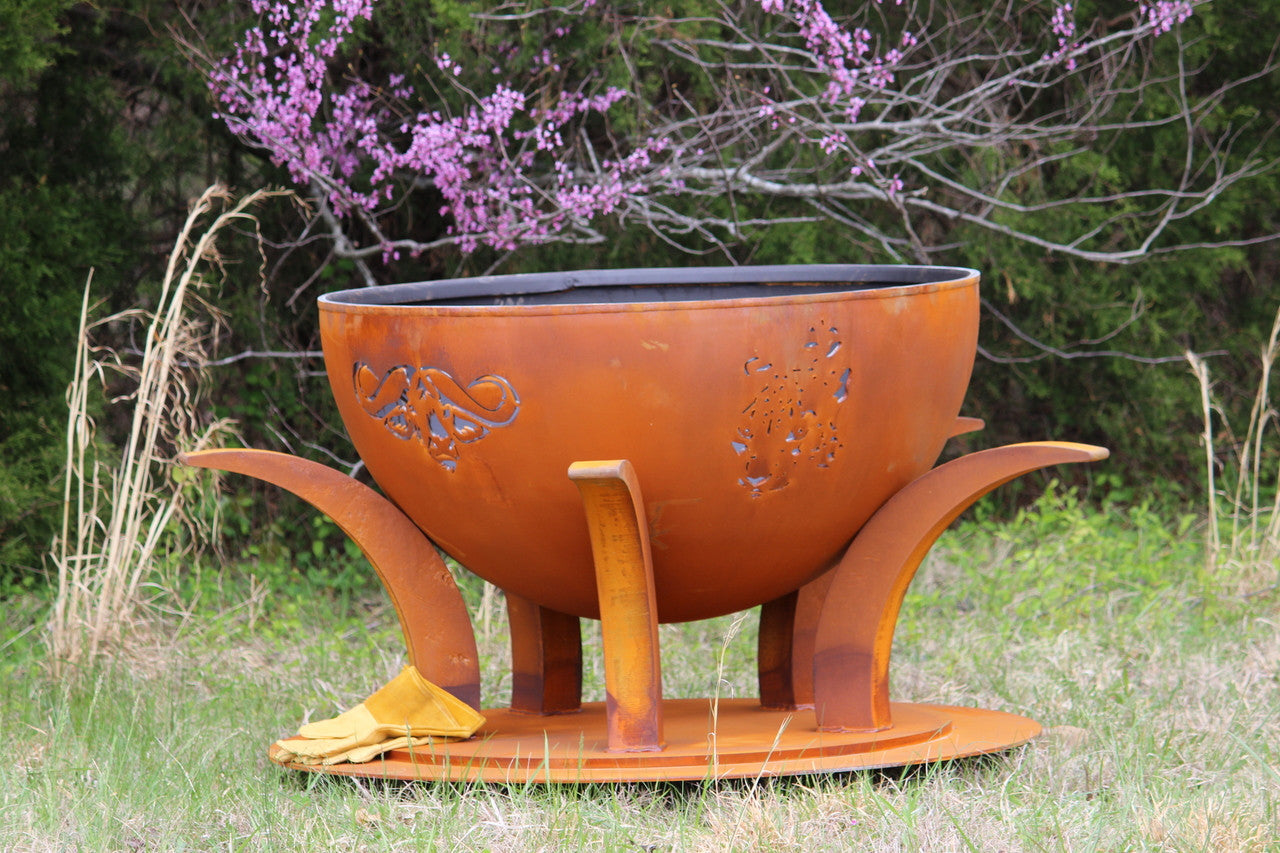 Rust-colored metal fire pit with decorative design in a natural setting