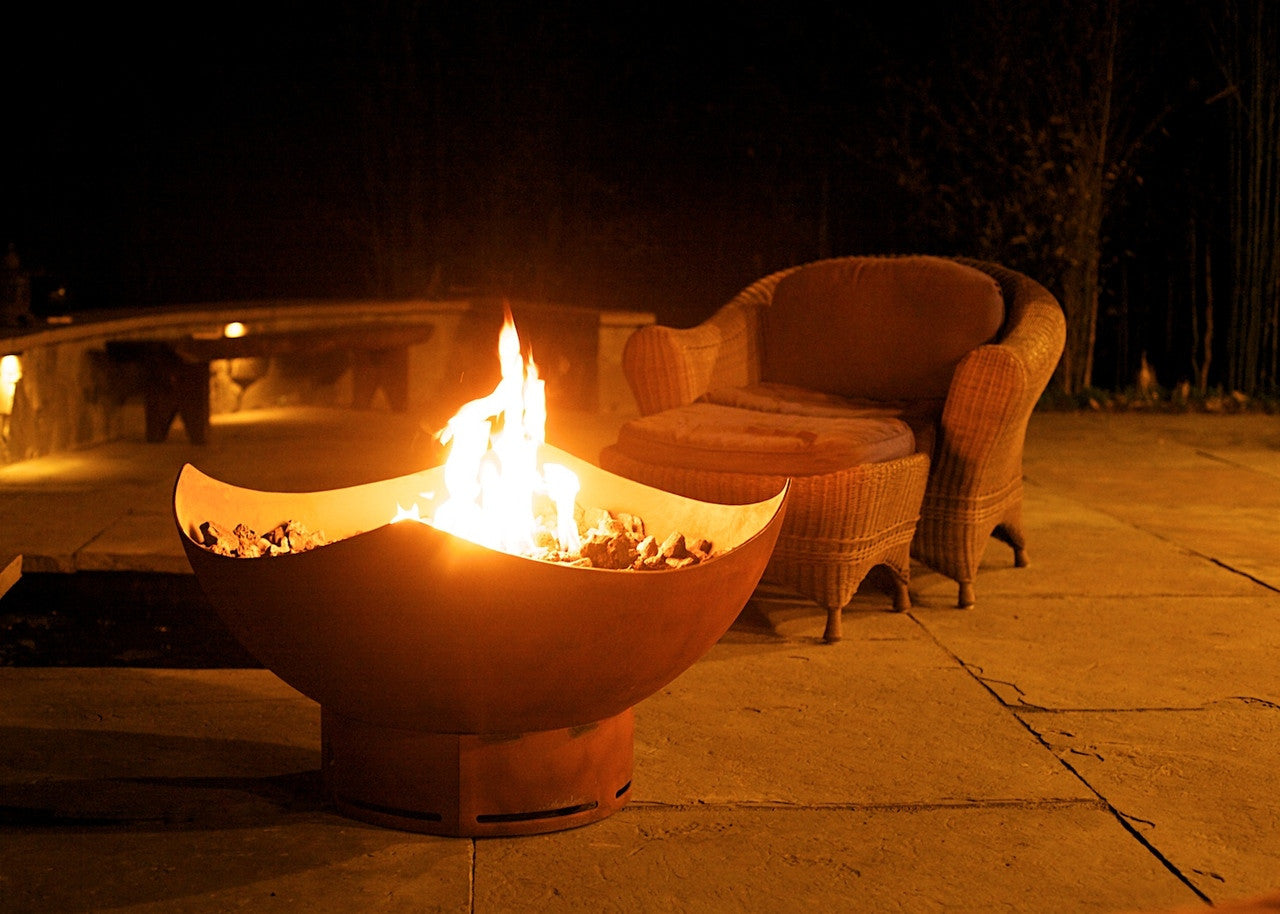 Fire pit bowl with flames outdoor setting with wicker furniture.