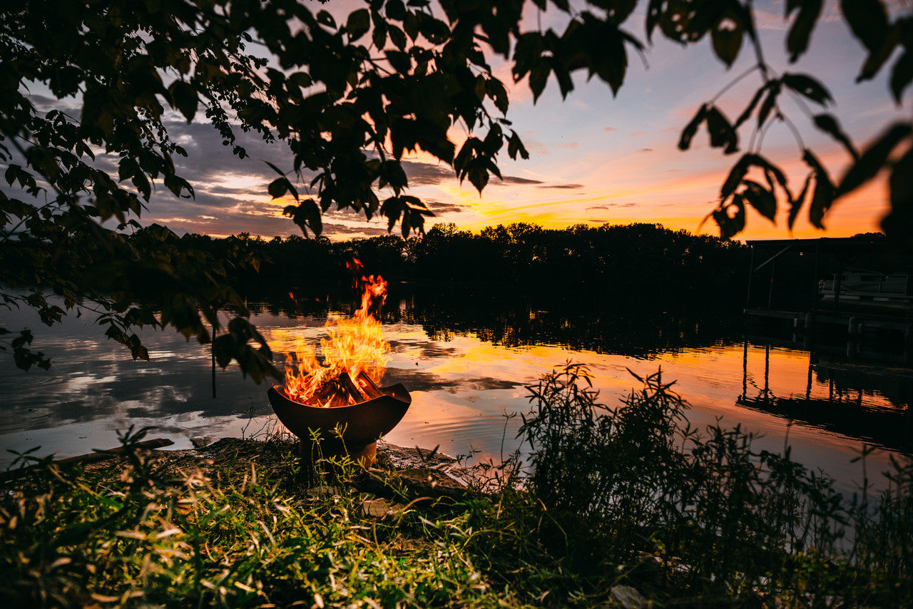 Fire pit by a lake at sunset with trees and water in the background