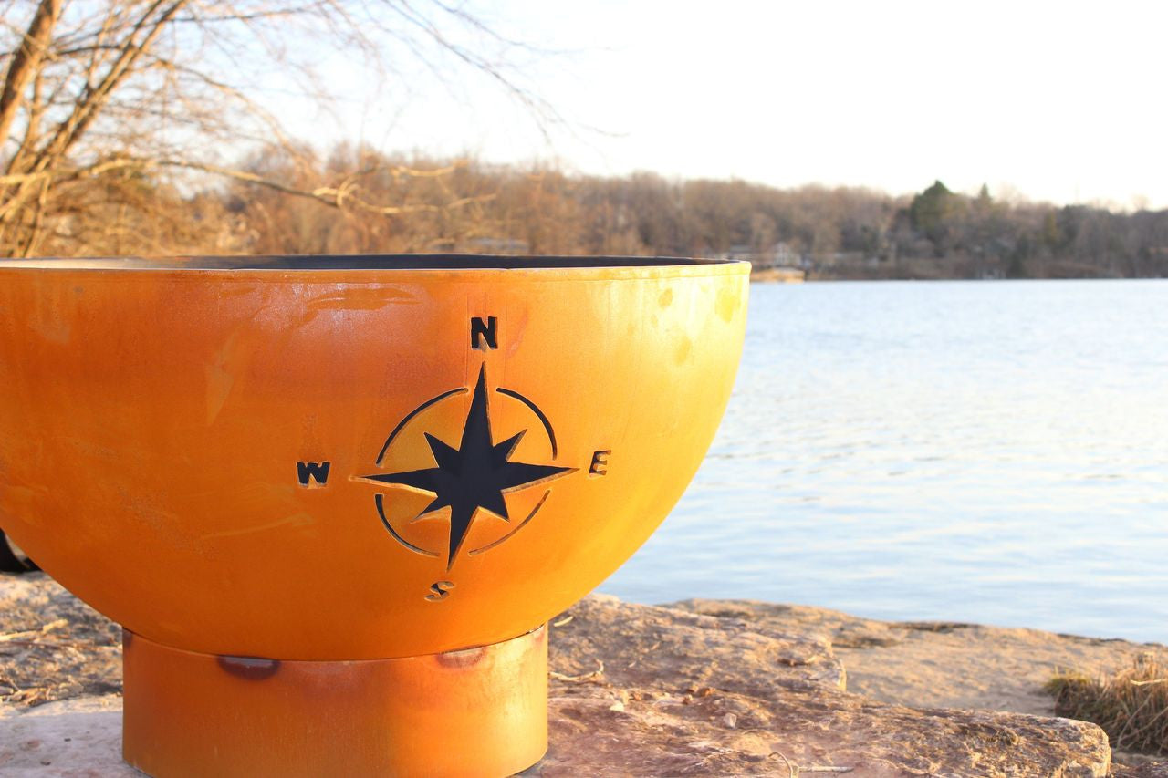 Orange fire pit with a compass design by a lake