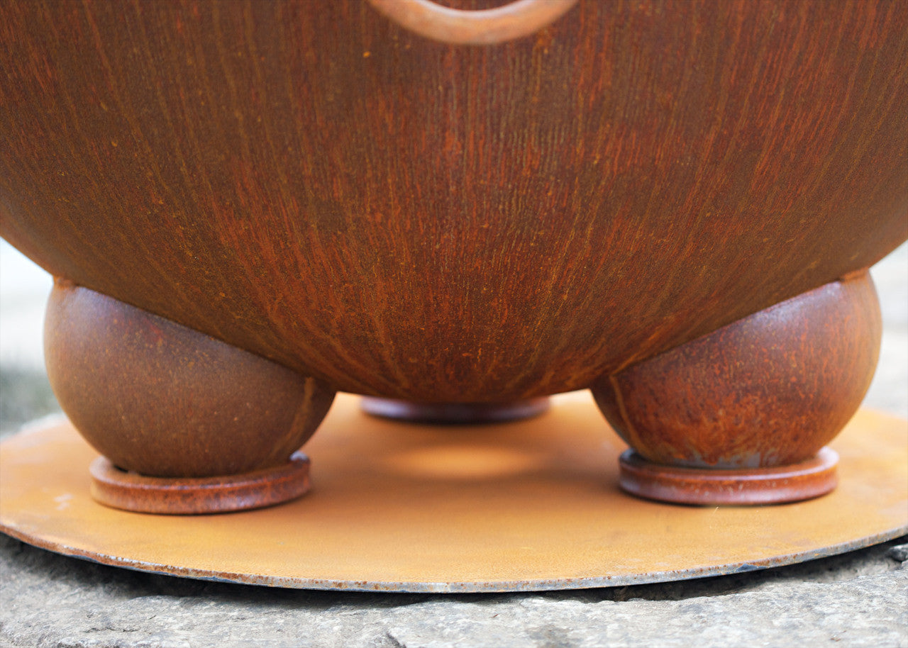 Close-up of a brown ceramic fire pit bowl with three feet on a stone surface