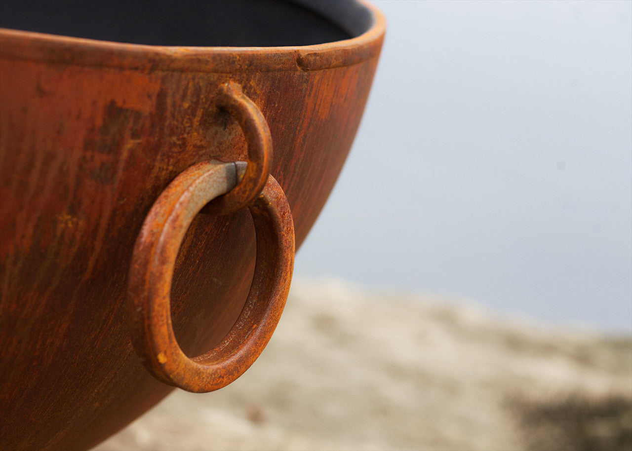 Wooden fire pit bowl with a circular handle on a blurred natural background