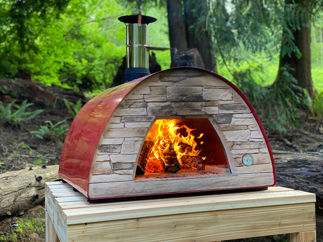 Wood-fired oven with flames inside, set against a natural outdoor background.