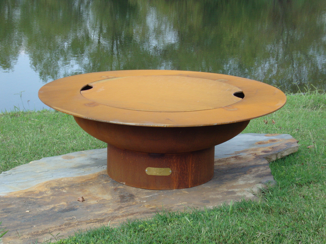 Rust-colored fire pit on a stone platform by a body of water