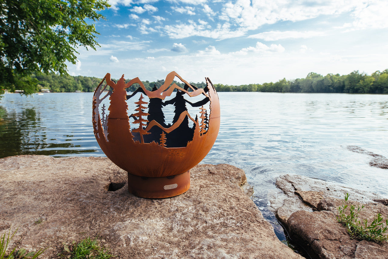 Decorative metal fire pit with nature design on a rock by a lake
