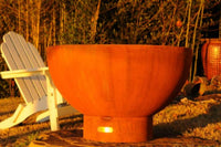 Rust-colored fire pit in a garden setting with a white chair and lanterns.
