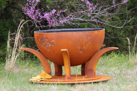 Rust-colored metal fire pit with decorative design in a natural setting