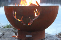 fire pit with antler design by a body of water outside with flaming fire