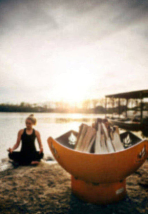Person meditating by a lake with a fire pit filled with wood