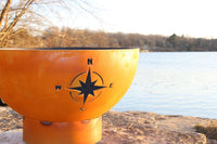 Orange fire pit with a compass design by a lake
